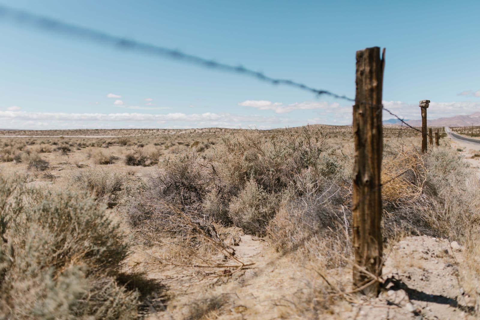 Barbed-wire fence line running along an open desert highway corridor with dry sagebrush and distant hills, the US-50 landscape at Mound House.