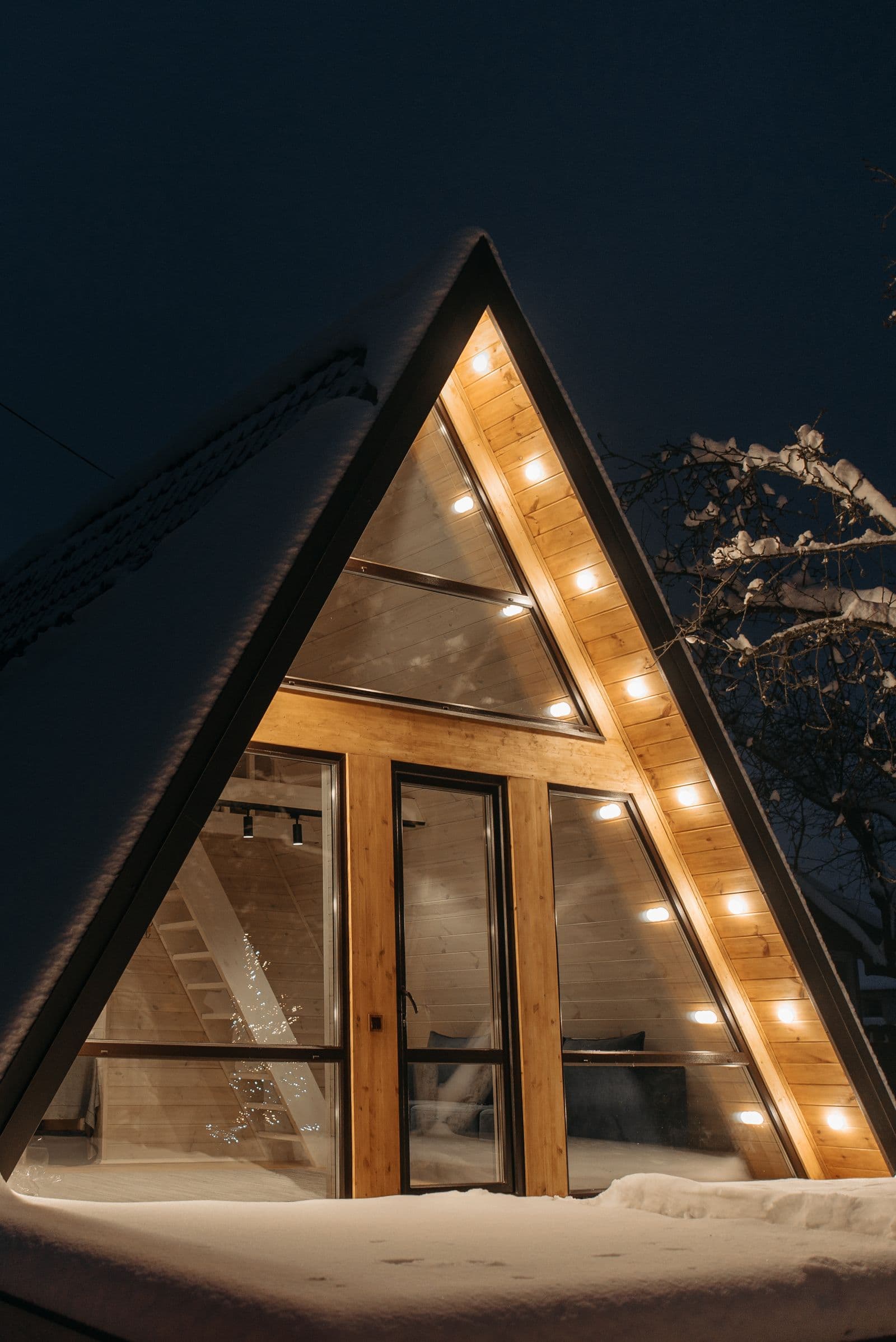 Warm white holiday lights glowing along the roofline of a snow-covered home at night, professionally installed holiday lighting.