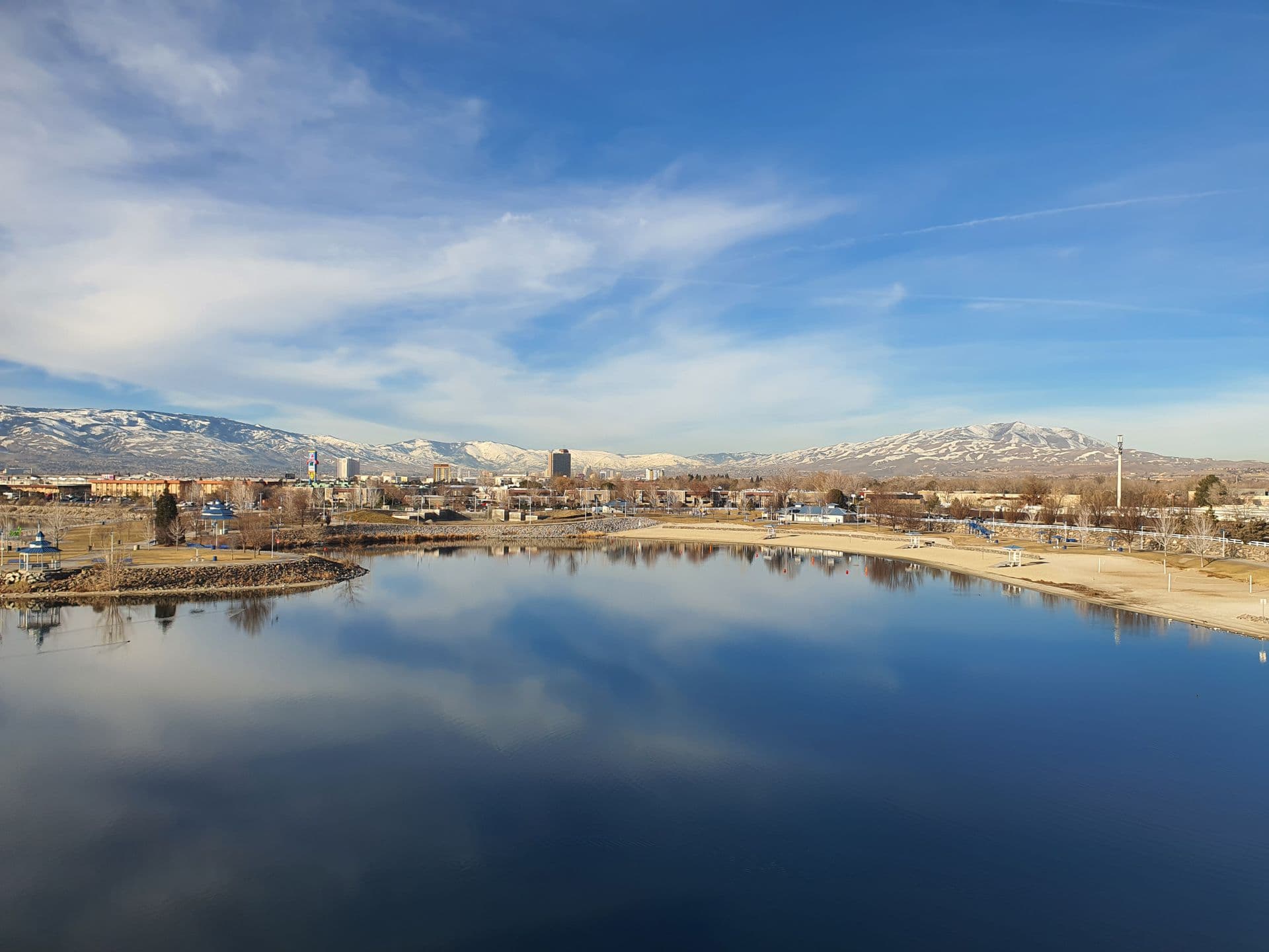 The Reno, Nevada skyline with snow-capped Sierra Nevada peaks behind it, reflected in still water. Still Window Co cleans windows across this valley.