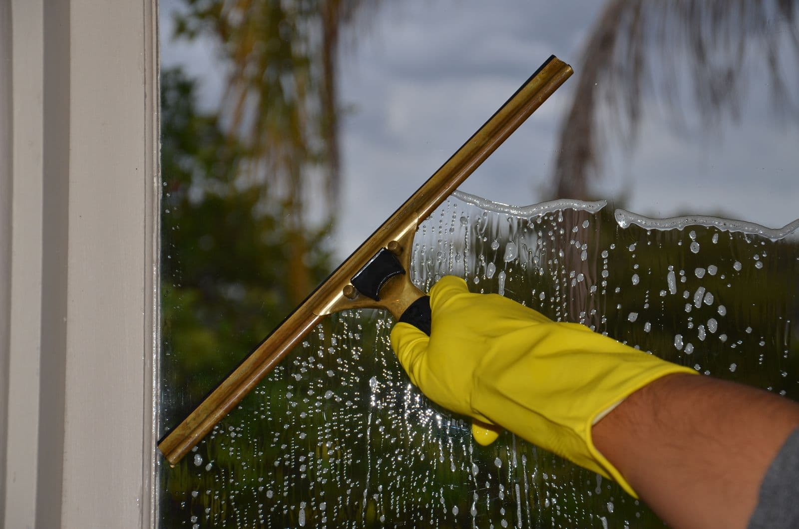 Close-up of a squeegee pulling water down glass covered in mineral spotting, the hard water staining common on Northern Nevada windows.